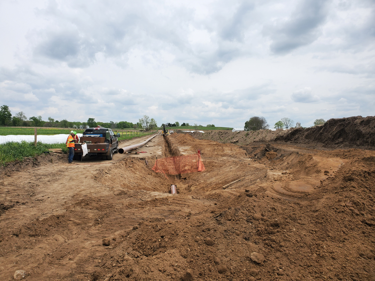 Workers inspect utility infrastructure as part of the Shipshewana Gas Line project, with visible construction equipment and a trench for gas line installation.