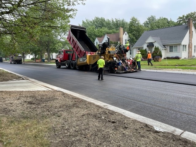 Road rehabilitation crew resurfacing Reynolds Street in Muskegon Heights, Michigan, with heavy equipment.