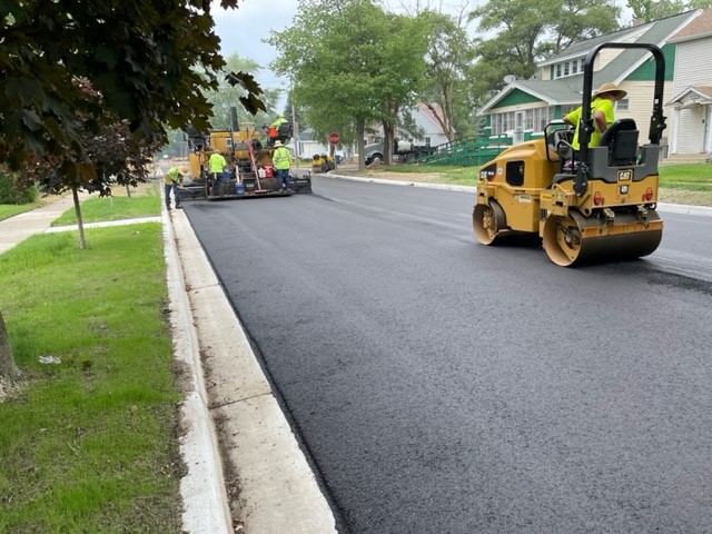 Construction workers paving Maffett Street in Muskegon Heights, showing smooth new asphalt and sidewalk work.