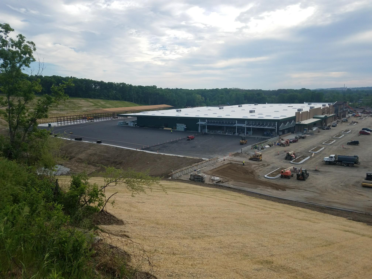 Aerial view of building construction progress at the Menards Commercial Development site, showing asphalt paving and construction equipment.