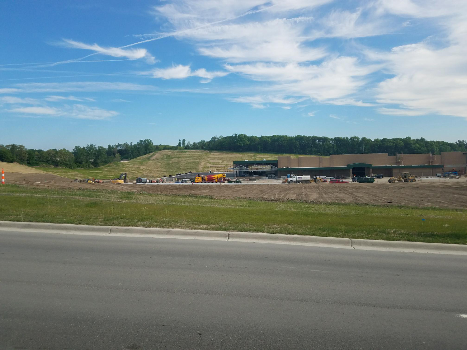 Wide view of the Menards construction site, showing newly graded slopes, parking lot development, and building structures.